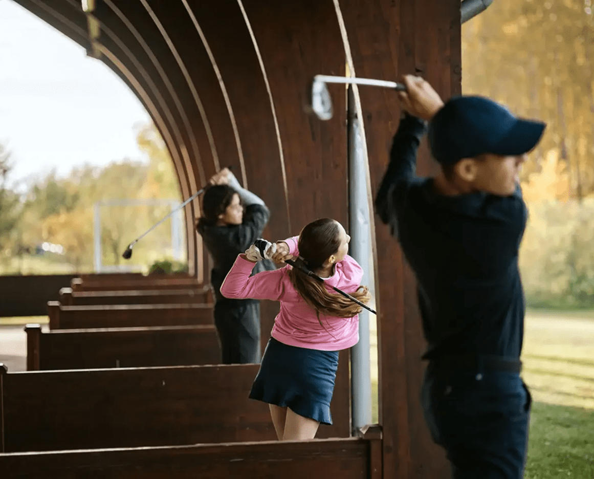 Three people practicing golf swings outdoors.